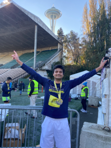 Moeez posing with arms up in number one fingers, with the space needle in the foreground. 